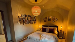 Une chambre à coucher avec un grand lit, un banc, un mur recouvert de photos encadrées et un luminaire suspendu.