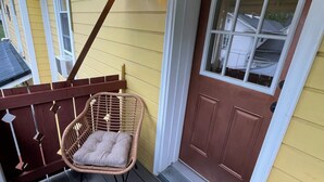 Une véranda couverte avec des fauteuils en osier et une table, une porte marron et un mur jaune.