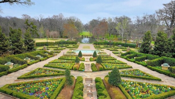 A formal garden with symmetrical pathways, manicured hedges, and a central water feature.