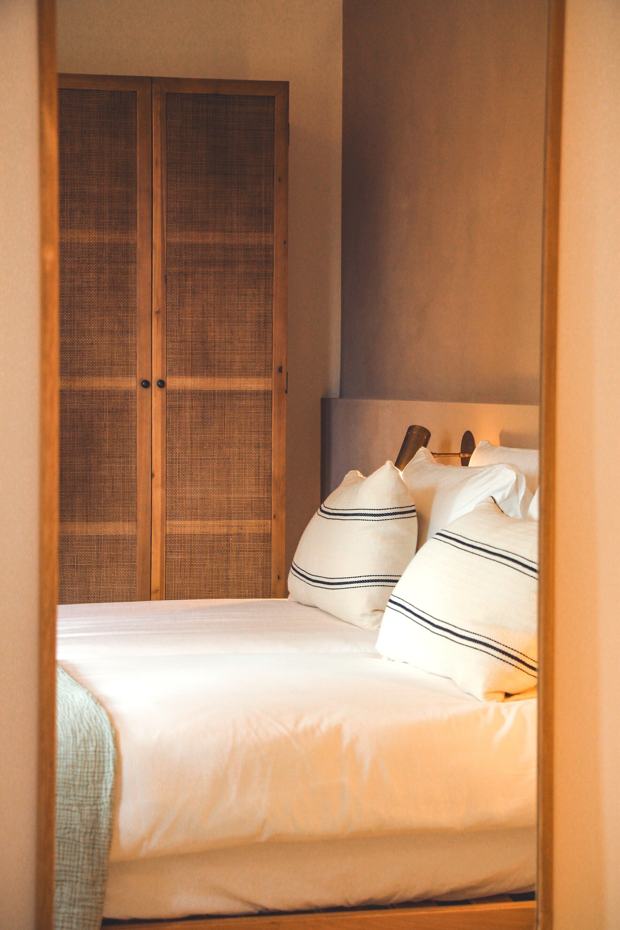 Een slaapkamer met een bed, kussens en een houten garderobe.