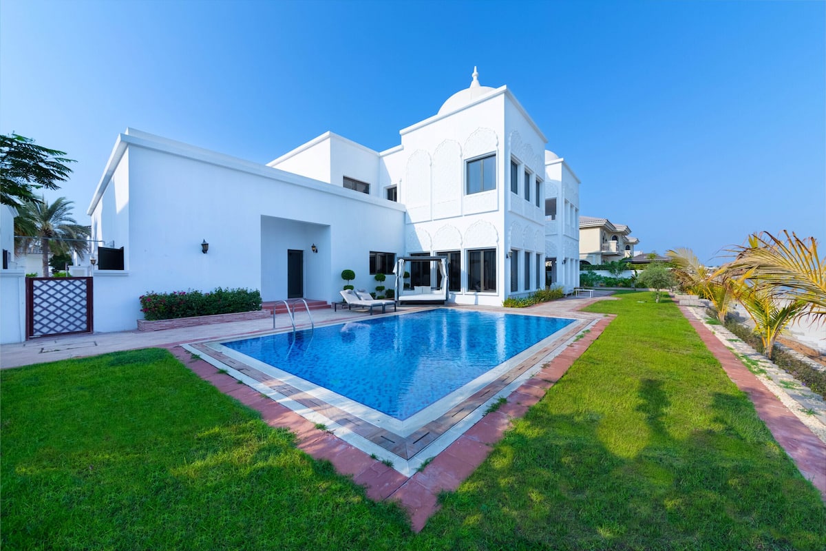 A modern white house with a swimming pool, a well-maintained lawn, and a clear blue sky.