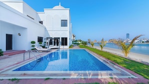 A swimming pool with a clear view of the sea, a white building with a dome, and a palm tree-lined pathway.