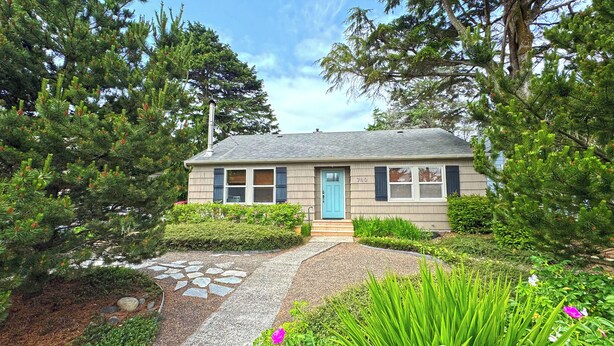 A single-story house with a blue door, surrounded by dense greenery and trees. - Georgie's Tide and True Cottage at Seaside Beach (Seaside)