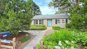 A house with a stone pathway leading to the front door, surrounded by lush greenery and flowering plants.