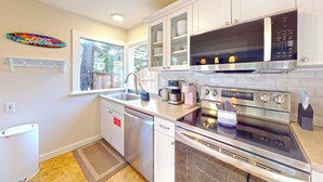 A modern kitchen with white cabinets, a microwave, an oven, a coffee maker, and a dishwasher. - Georgie's Tide and True Cottage at Seaside Beach (Seaside)