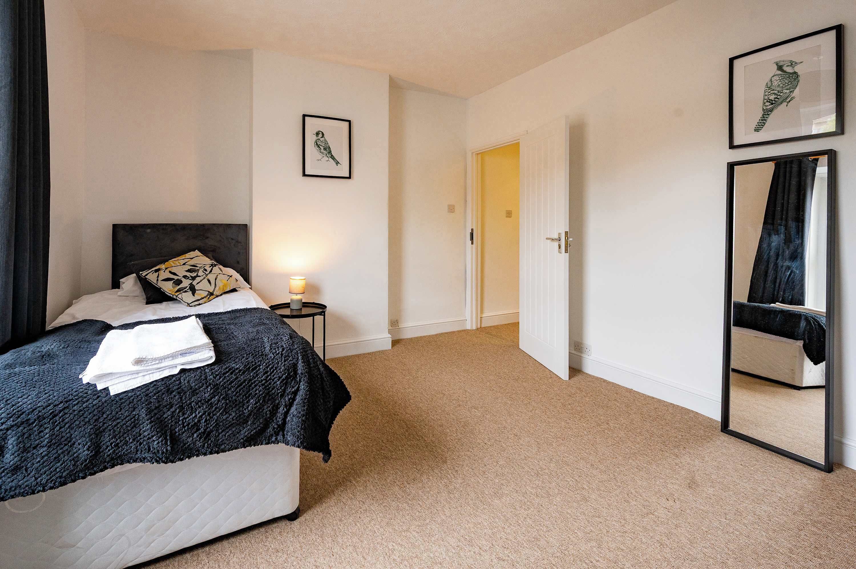 A bedroom with a bed, a bedside table with a lamp, a door, and two framed pictures on the wall.