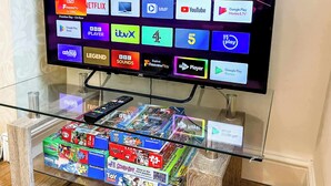 Ein Fernseher zeigt verschiedene Streaming-Apps, darunter eine Sammlung von Kinderspielzeug auf einem Glastisch darunter.