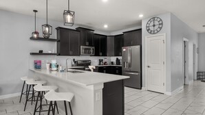 A modern kitchen with dark cabinets, a large island with bar stools, stainless steel appliances, and pendant lighting.