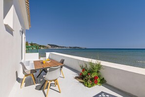 A balcony with a table and chairs overlooking a clear blue sea and a distant hill.