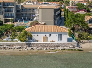 A coastal building with a tiled roof, a stone wall, and a beach in the foreground.