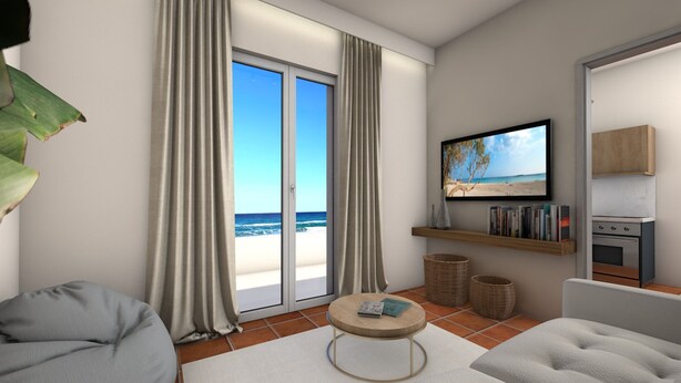 Een moderne woonkamer met een groot raam dat uitkijkt op een strand, een flatscreen televisie, een boekenkast en een keukenhoek.