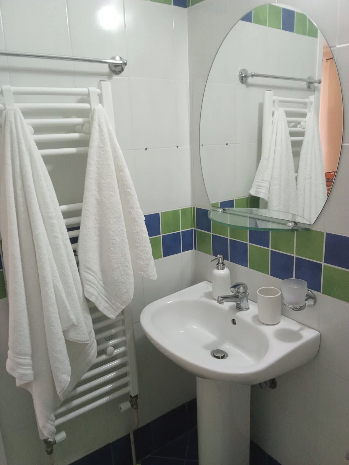 A bathroom with a white sink, a mirror, and a towel rack with multiple white towels.