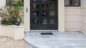 Une entrée moderne avec une porte noire, un auvent en verre et un petit jardin agrémenté de fleurs rouges.