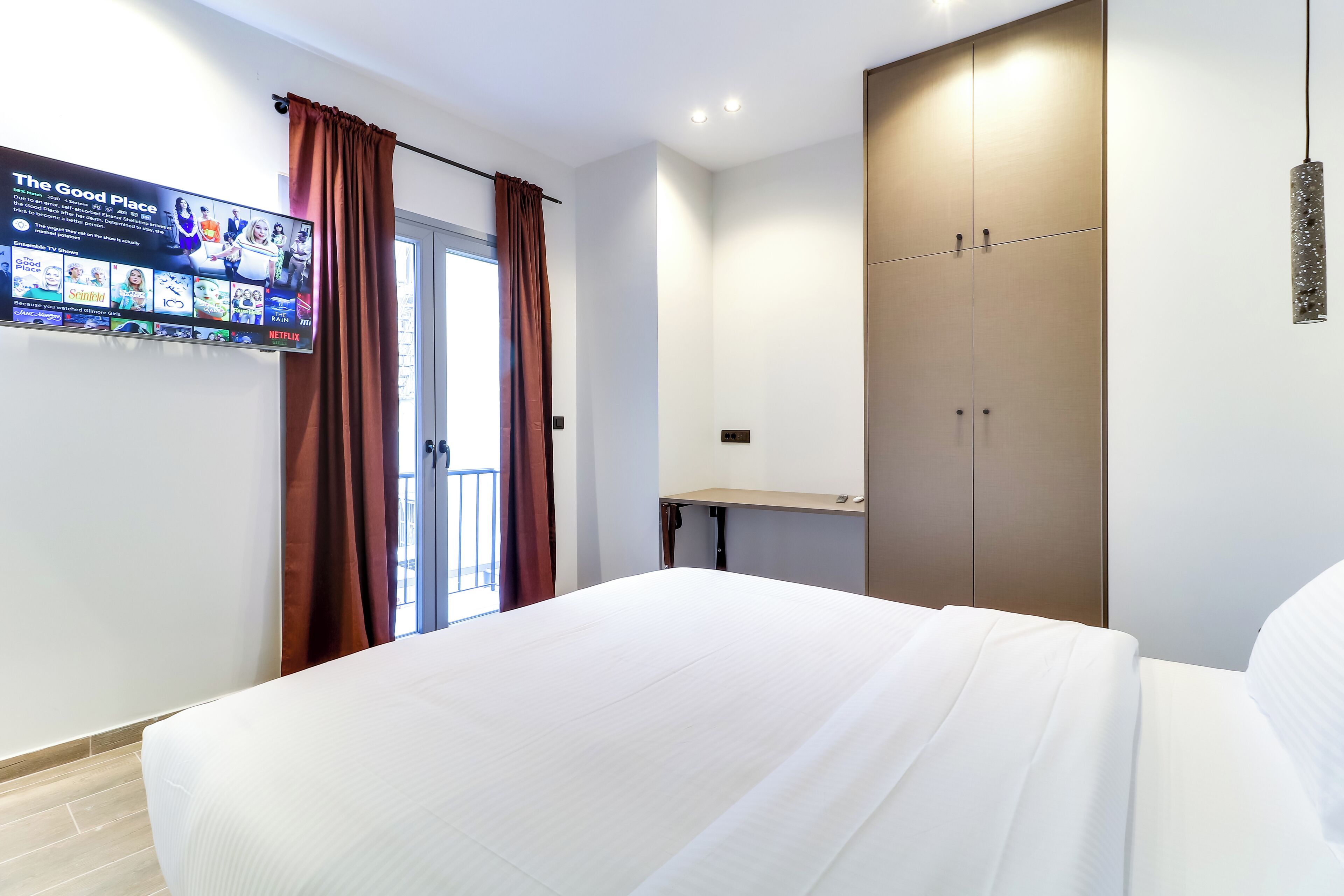 A hotel room with a bed, a wardrobe, a desk, and a TV displaying a channel guide.