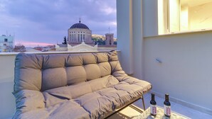 Un balcon avec un canapé confortable, deux bouteilles de vin et une vue sur un bâtiment surmonté d’un dôme.