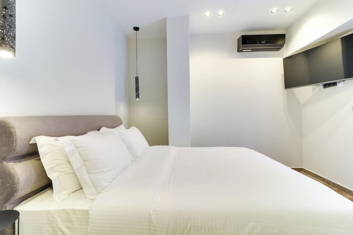 Une chambre moderne avec un grand lit, un téléviseur fixé au mur et un luminaire suspendu.
