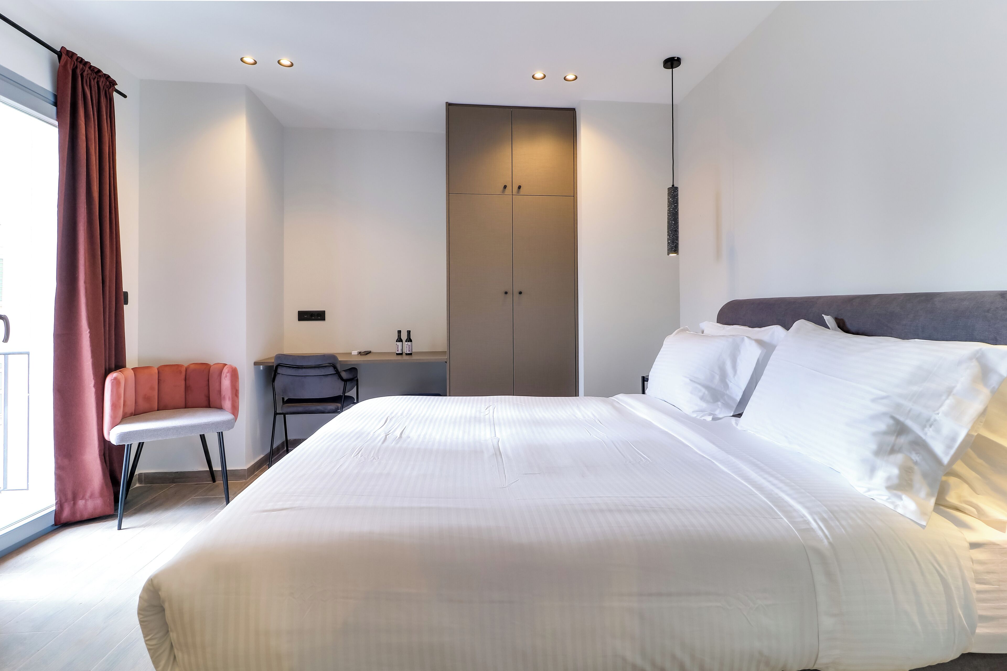 A modern hotel room with a large bed, a desk, and a wardrobe.