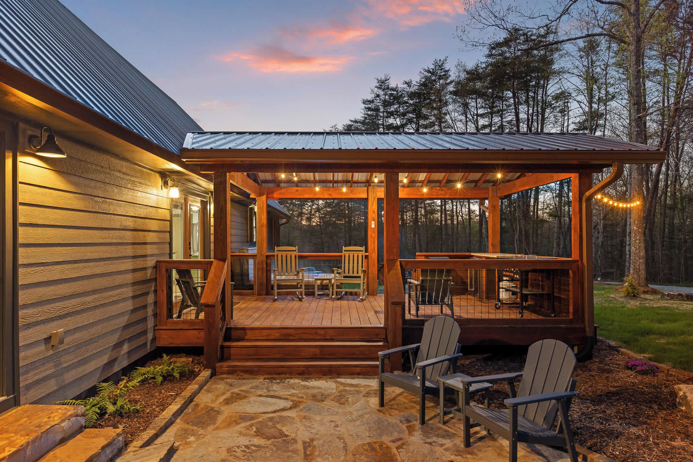 Una terraza de madera con mobiliario exterior y una zona cubierta, rodeada de árboles.