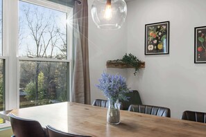 A dining area with a wooden table, chairs, a vase with flowers, a hanging light fixture, and framed botanical prints on the wall. - Hemlock Haven – Perfect for Groups of 16 (Pikeville)