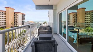 A balcony with wicker furniture, a glass railing, and a view of other buildings and the sea. - San Remo 304 2BR Beachfront Condo (Redington Shores)