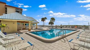 A rooftop pool with lounge chairs, a covered seating area, and palm trees. - San Remo 304 2BR Beachfront Condo (Redington Shores)