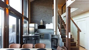 A modern kitchen with a stone backsplash, a dining area with a table and chairs, and a staircase leading to an upper level. - Villa Halla 2, HimosYkkösen alue (Jämsä)