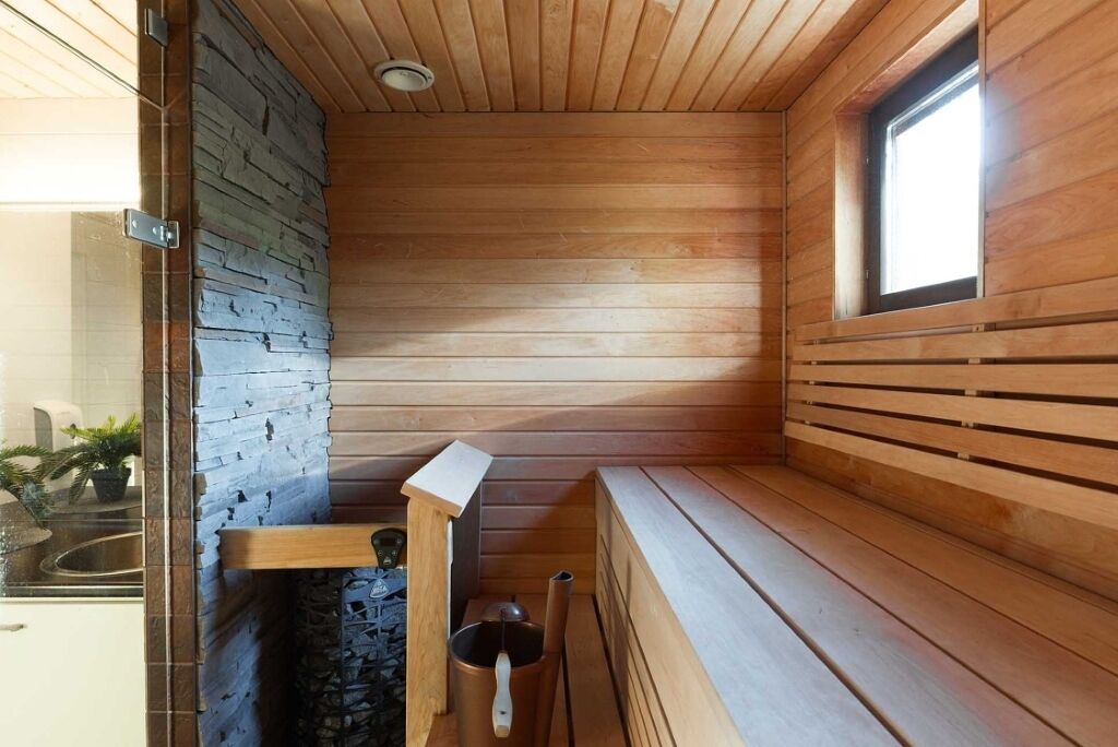 Sauna, jossa on puuseinät, penkki, ikkuna ja kiviseinä.