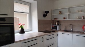 A modern kitchen with white cabinets, a black oven, a microwave, and a sink. There is a window with a view of a brick wall outside.