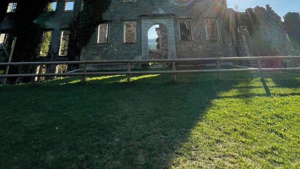 An old stone building with a central archway and multiple windows, surrounded by a grassy area.