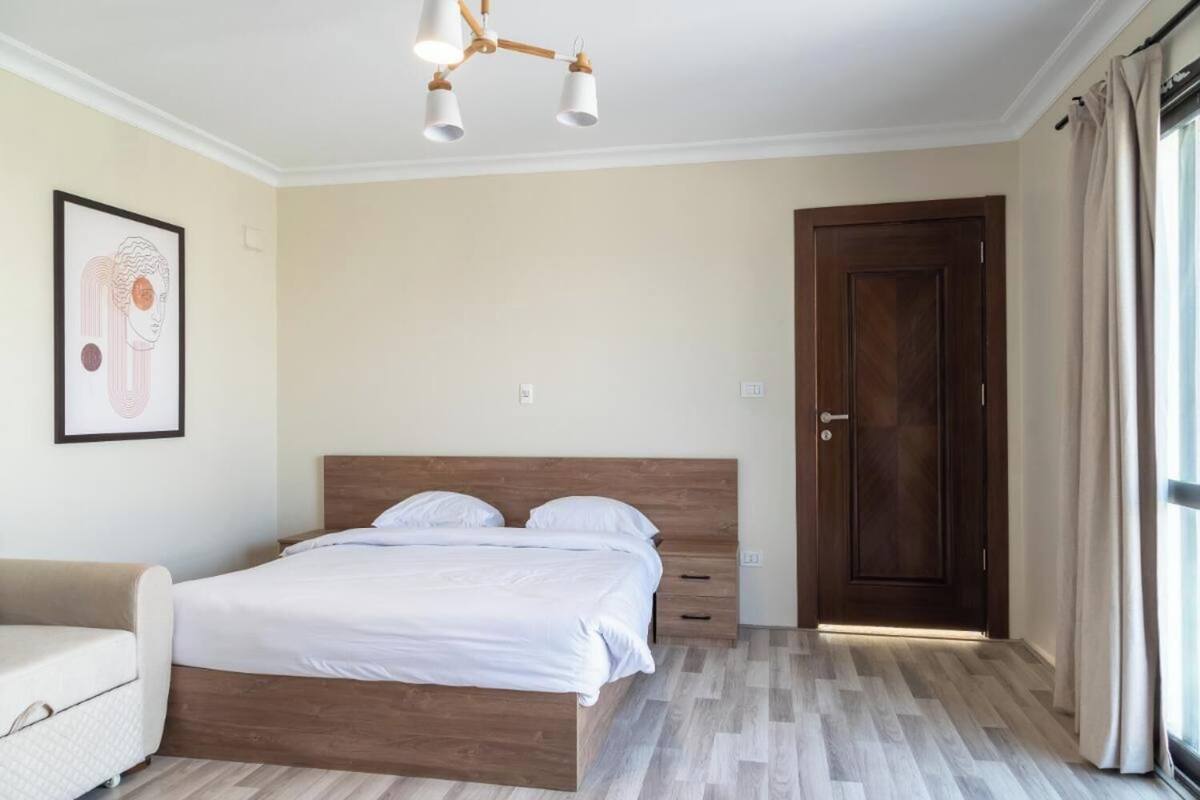 A bedroom with a wooden bed, a bedside table, a chair, a framed picture on the wall, and a door.