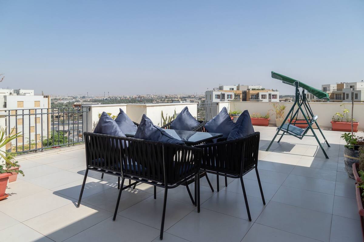 A rooftop terrace with a table and chairs, a telescope, and potted plants.