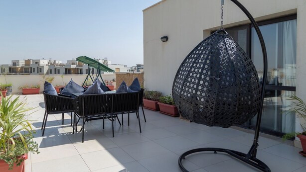 Un patio en la azotea con una silla colgante, una mesa con sillas y plantas en macetas.