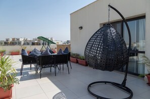 A rooftop patio with a hanging chair, a table with chairs, and potted plants. - Settle Inn Sodic Eastown Studio (New Cairo)