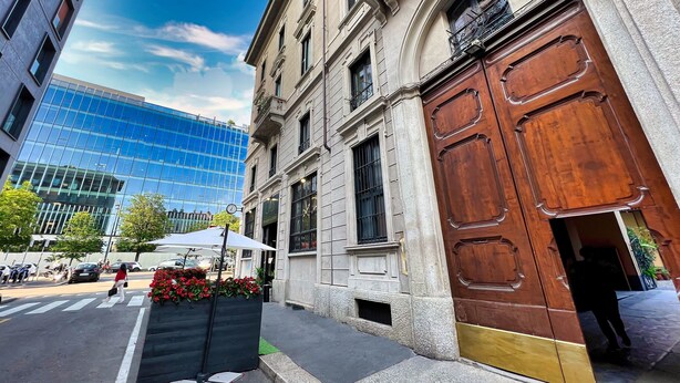 Vista de una calle con un edificio histórico que presenta una puerta de madera grande y un edificio moderno de vidrio al fondo.