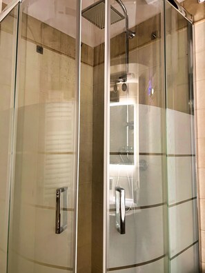 A glass-enclosed shower area with a handheld showerhead and a wall-mounted faucet.