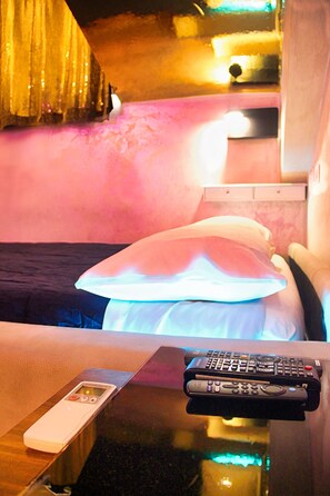 A hotel room with a bed, a nightstand, and a table with two remote controls.