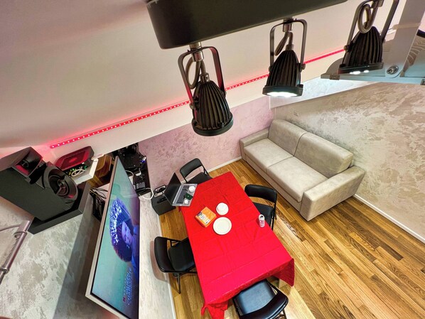 A modern room with a red table, a grey sofa, and a computer setup with a large monitor.
