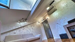 Una sala de estar moderna con sofá, piso de madera y techo alto con conductos y luminarias expuestos.