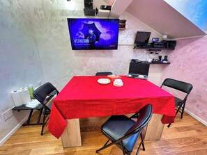 A conference room with a red table, black chairs, a TV displaying 'WEDNESDAY' series, and a laptop.