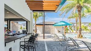 A poolside area with lounge chairs, a bar, and a pool. - Stylish Home,Themed Rooms, Pvt Pool, BBQ, Resort Amenities – Internacional Drive (Orlando)