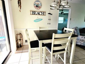 Een eethoek met een tafel, stoelen, een wandklok en een bord waarop 'BEACH' staat.