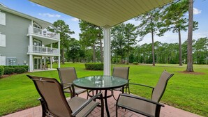 A patio with a glass table and four chairs, a covered area, and a two-story building with a balcony. - Relax, Beach, Golf, Shop, Repeat 2 Bedroom Resort (Calabash)