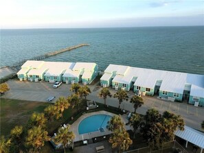Ett hotell vid kusten med flera ljusblå byggnader, en swimmingpool och en brygga som sträcker sig ut i havet.