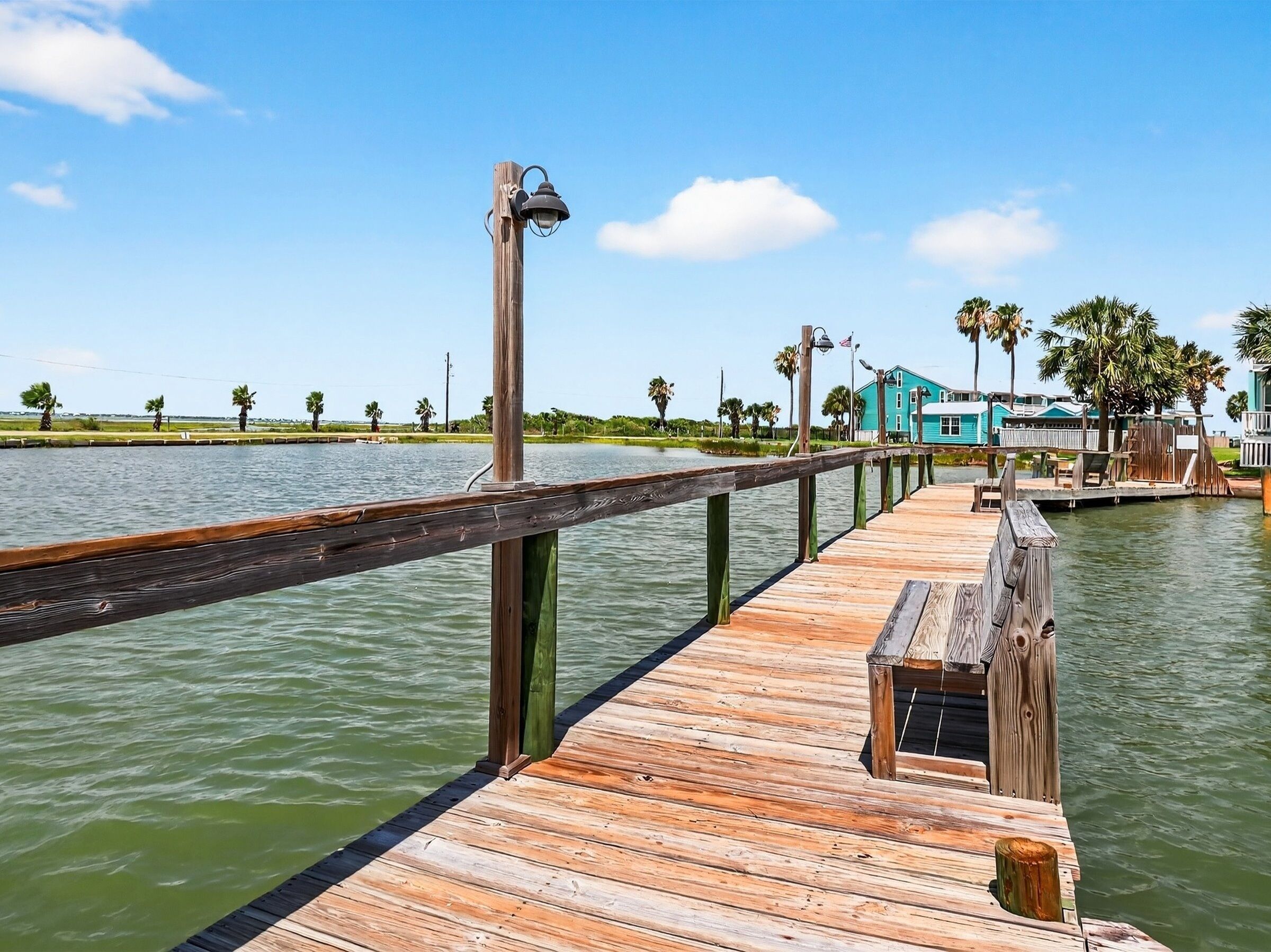 A wooden pier extending into a body of water, with a blue building in the background.