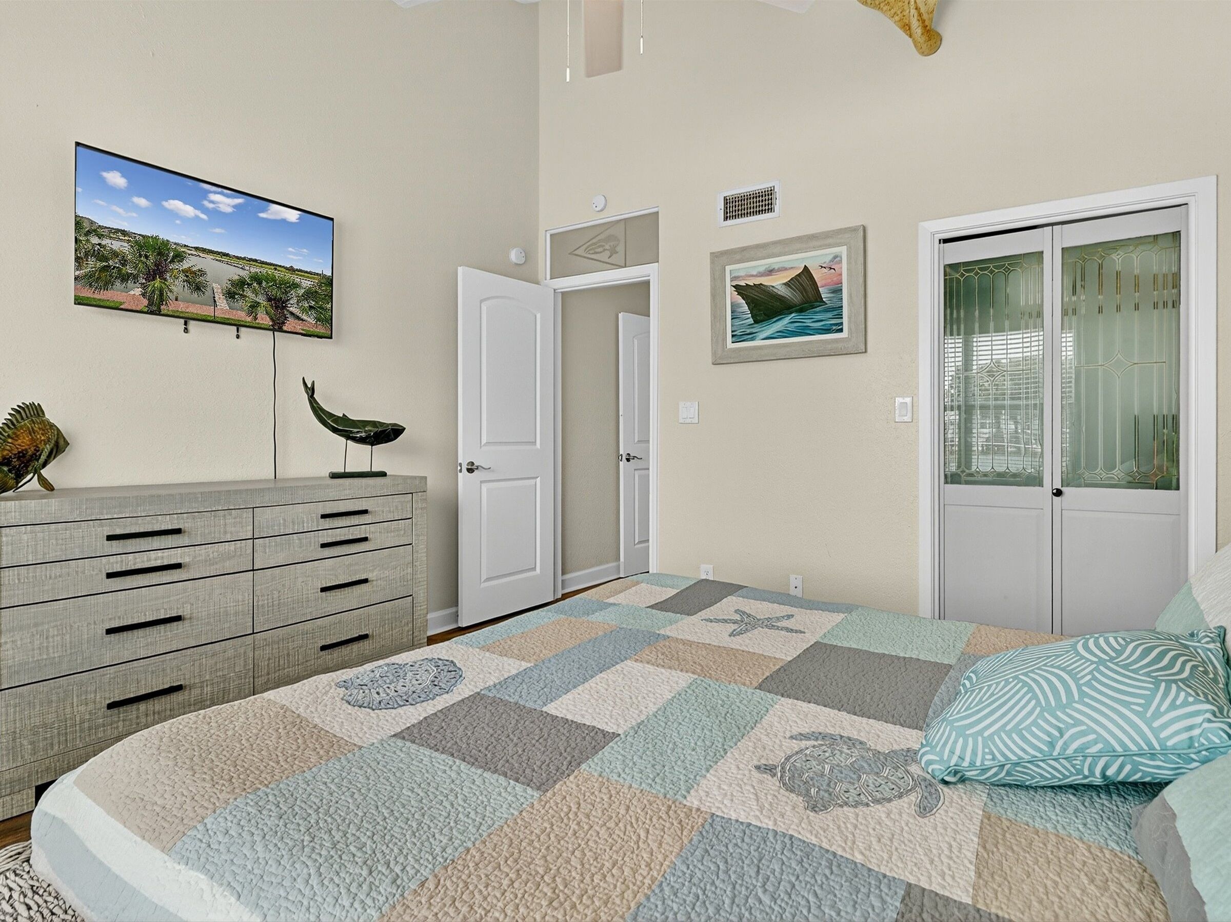 Un dormitorio con cama, cómoda, puerta y dos cuadros en la pared.