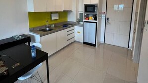 A modern kitchen with white cabinets, a black countertop, and a green backsplash. There is a small refrigerator, a microwave, and a sink. - Cassia 1bdr by ISI (Choeng Thale)