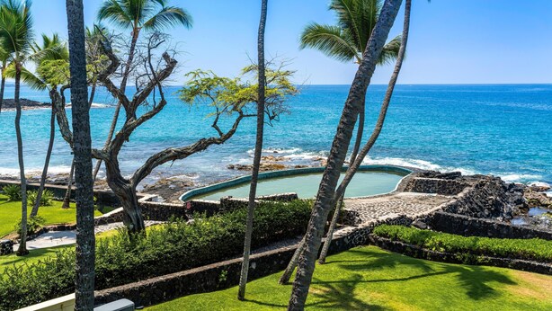 A tropical resort with a clear view of the ocean, palm trees, and a swimming pool area. - Big Island Kona Isle E32 1 Bedroom Condo (Kailua-Kona)