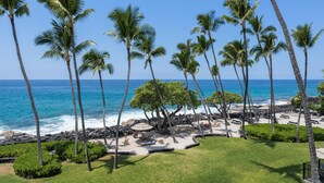 A beach resort with palm trees, a rocky shoreline, and a view of the ocean. - Big Island Kona Isle E32 1 Bedroom Condo (Kailua-Kona)