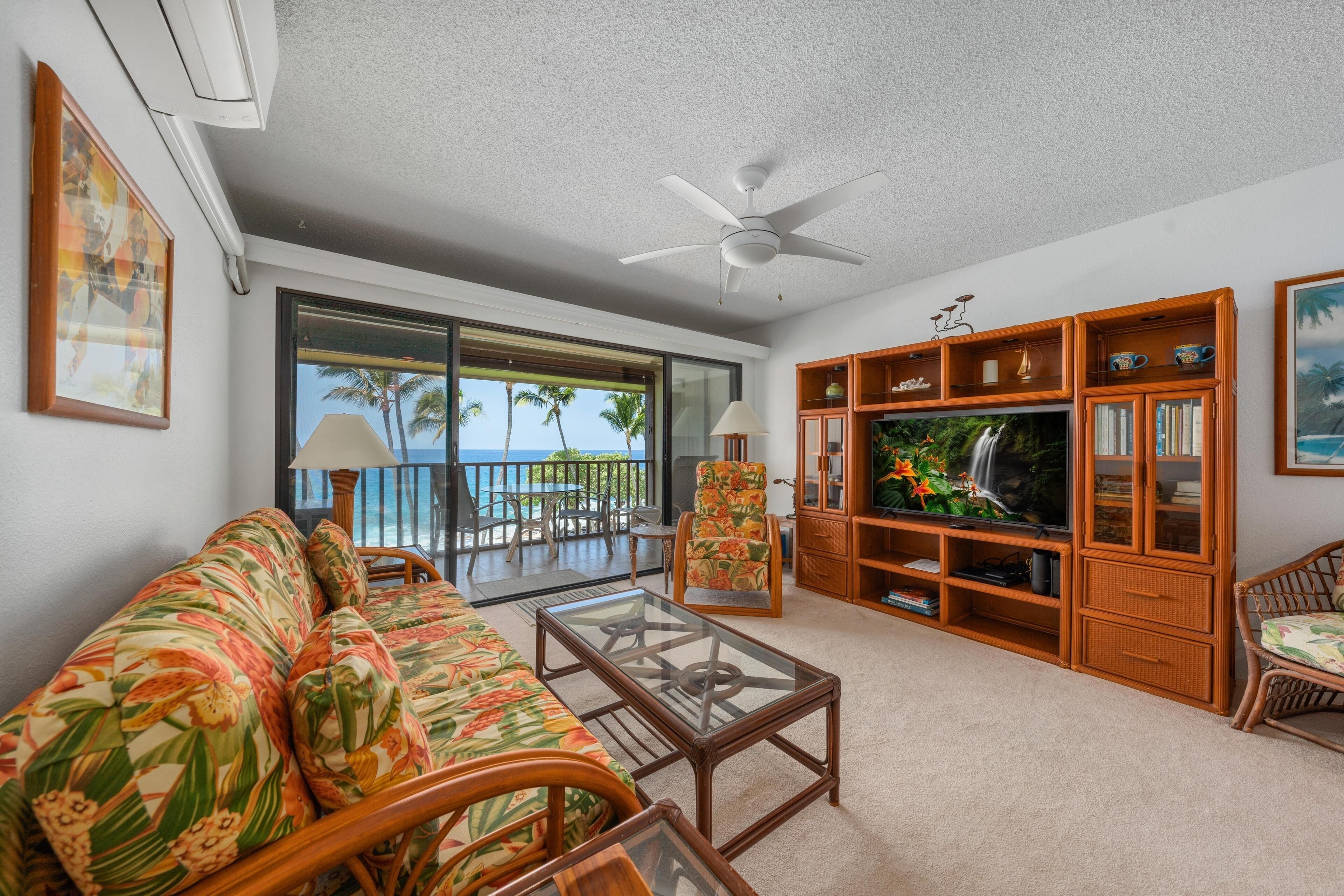 A living room with a sofa, coffee table, TV stand, and a ceiling fan.