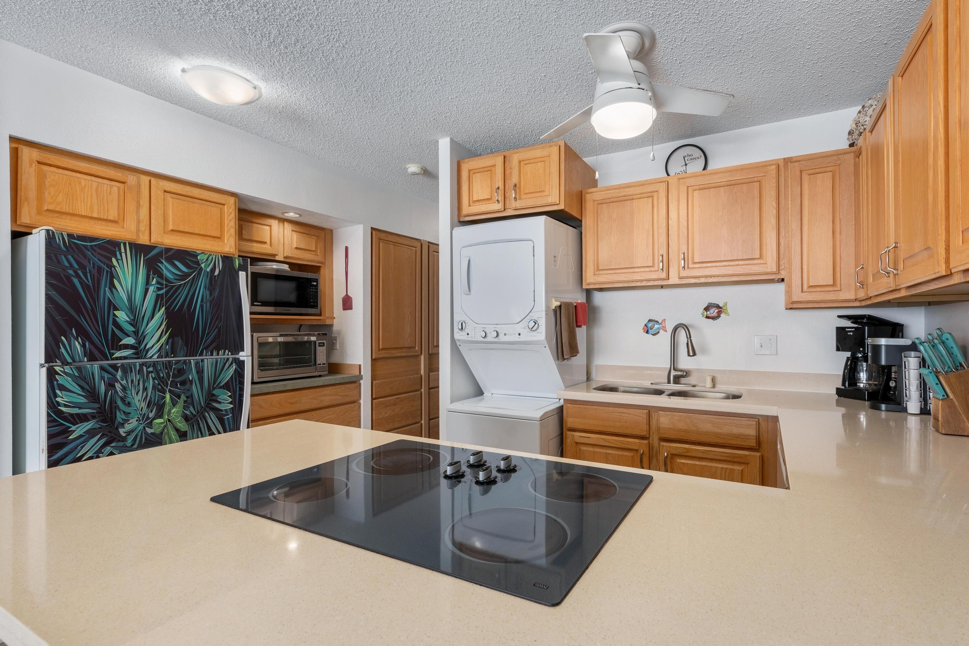 A modern kitchen with wooden cabinets, a black induction cooktop, a white refrigerator, a microwave, and a stove.